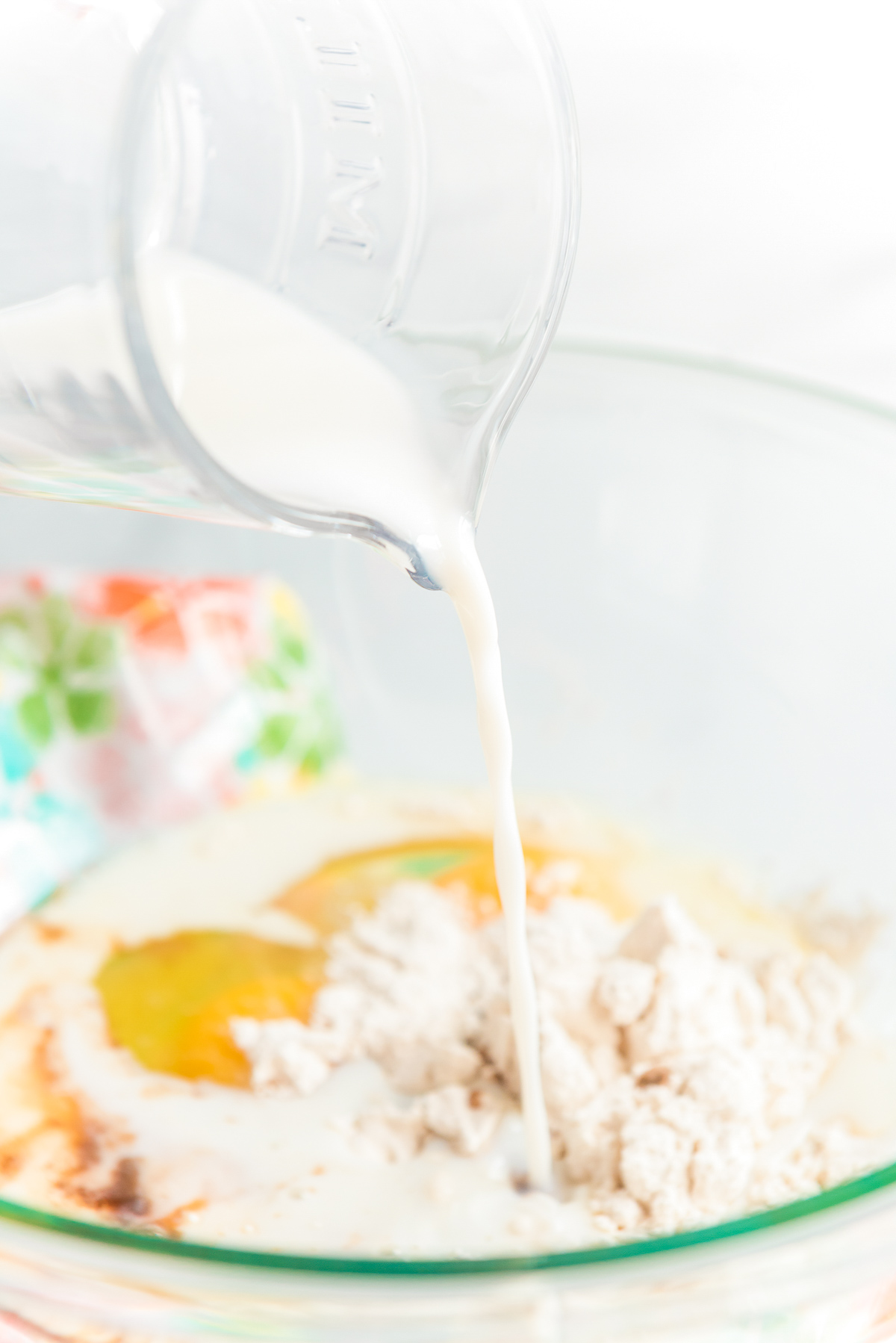 Milk being poured into a mixing bowl with eggs and flour.