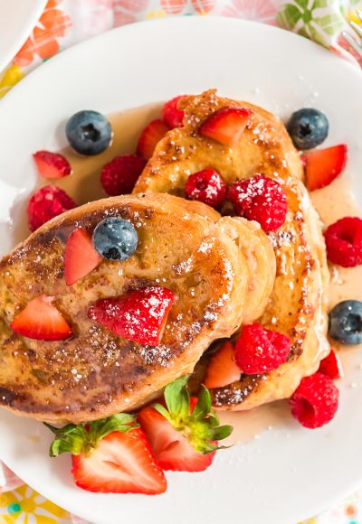 Overhead photo of French toast topped with berries and maple syrup on a white plate.