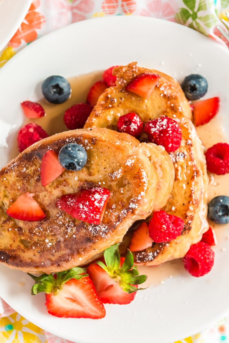 Overhead photo of French toast topped with berries and maple syrup on a white plate.