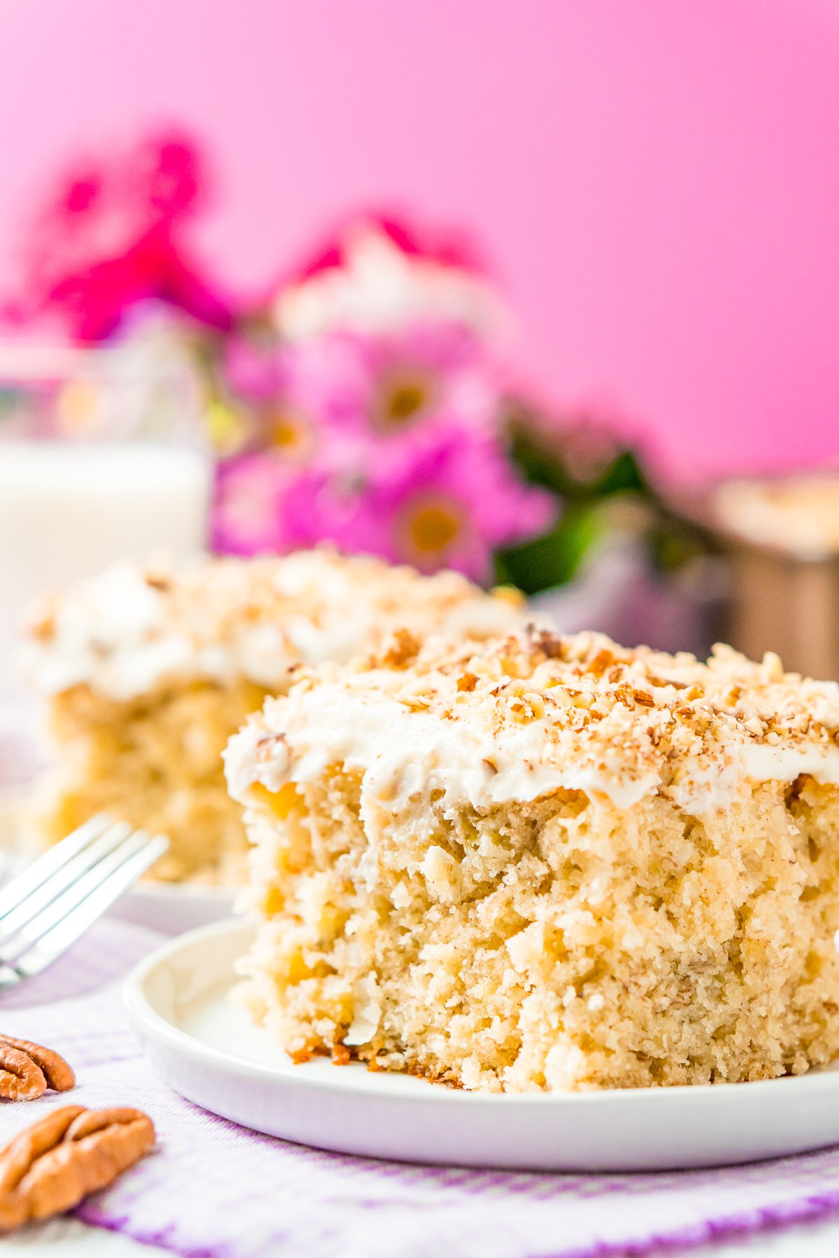 Slice of cake on a small white dessert plate with a pink background and flowers in the background.