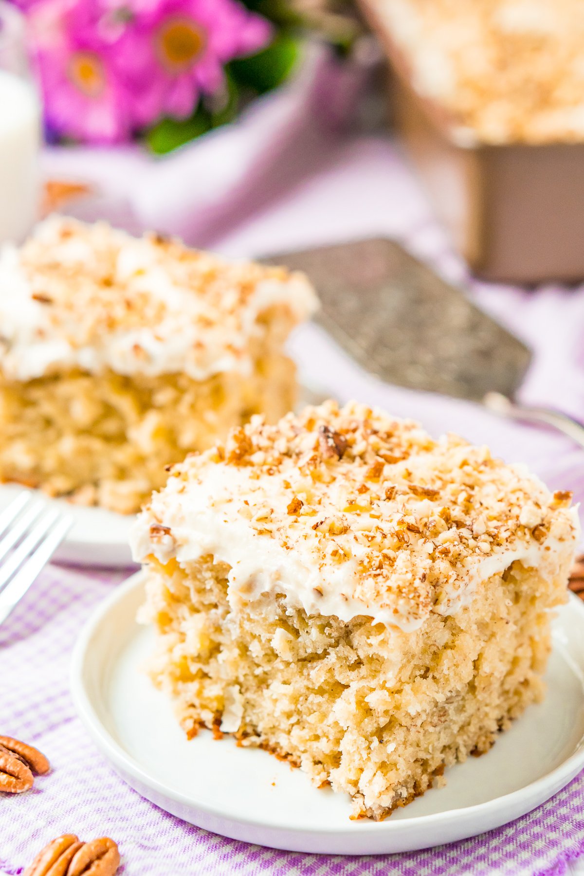 Two slices of cake topped with pecan pieces on white desserts plates.