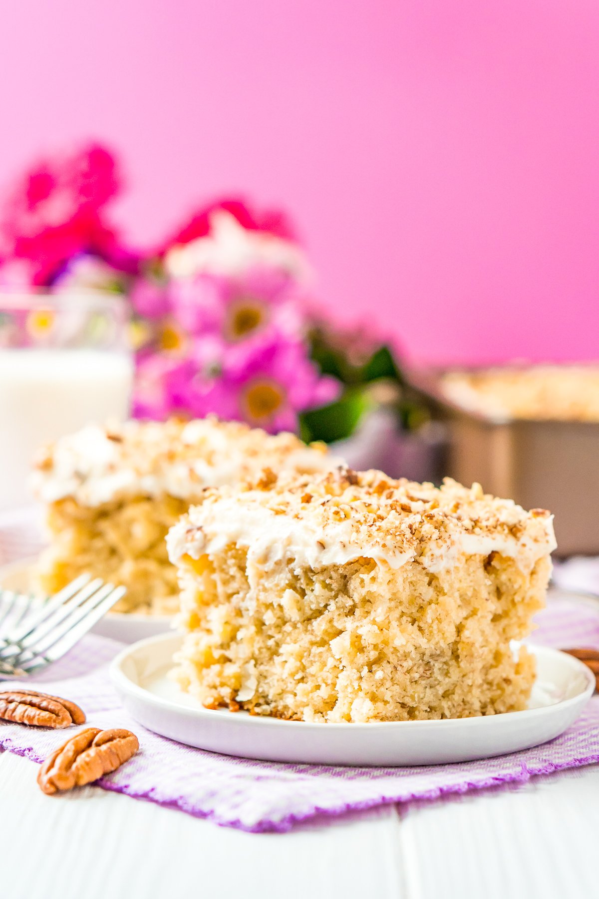 Two slices of hummingbird cake on small white dessert plates with a pink background.