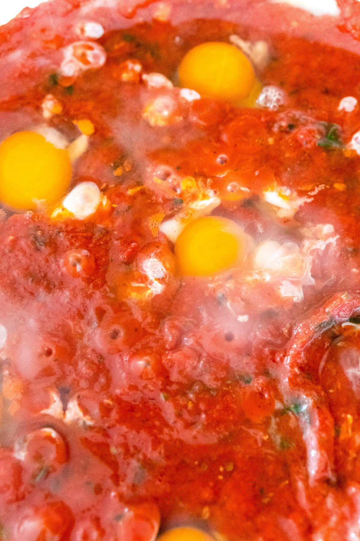 Close up photo of eggs being poached in tomato sauce.