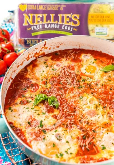 Italian Eggs In Purgatory in a skillet with cherry tomatoes and a carton of eggs in the background.