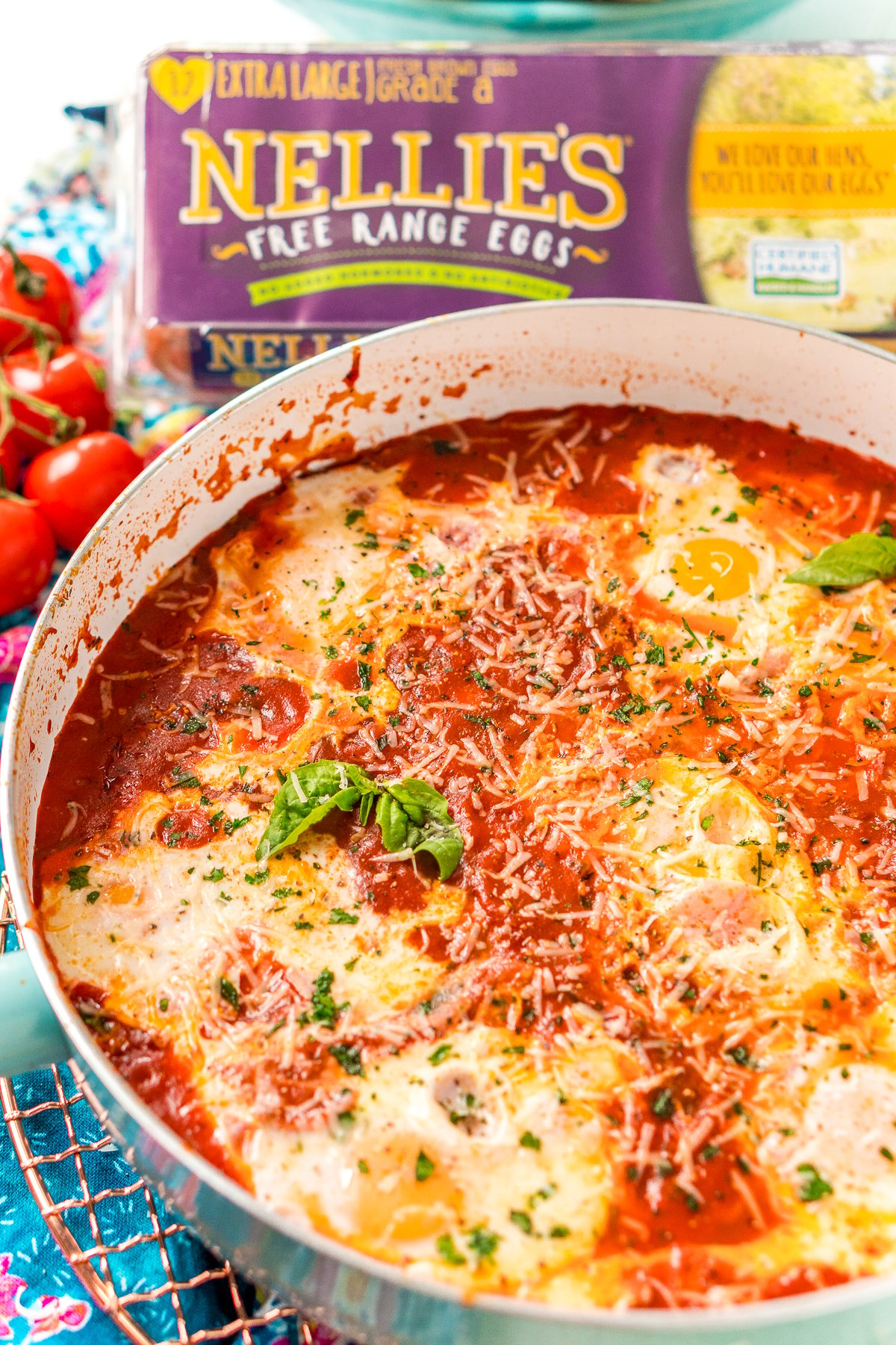 Italian Eggs In Purgatory in a skillet with cherry tomatoes and a carton of eggs in the background.