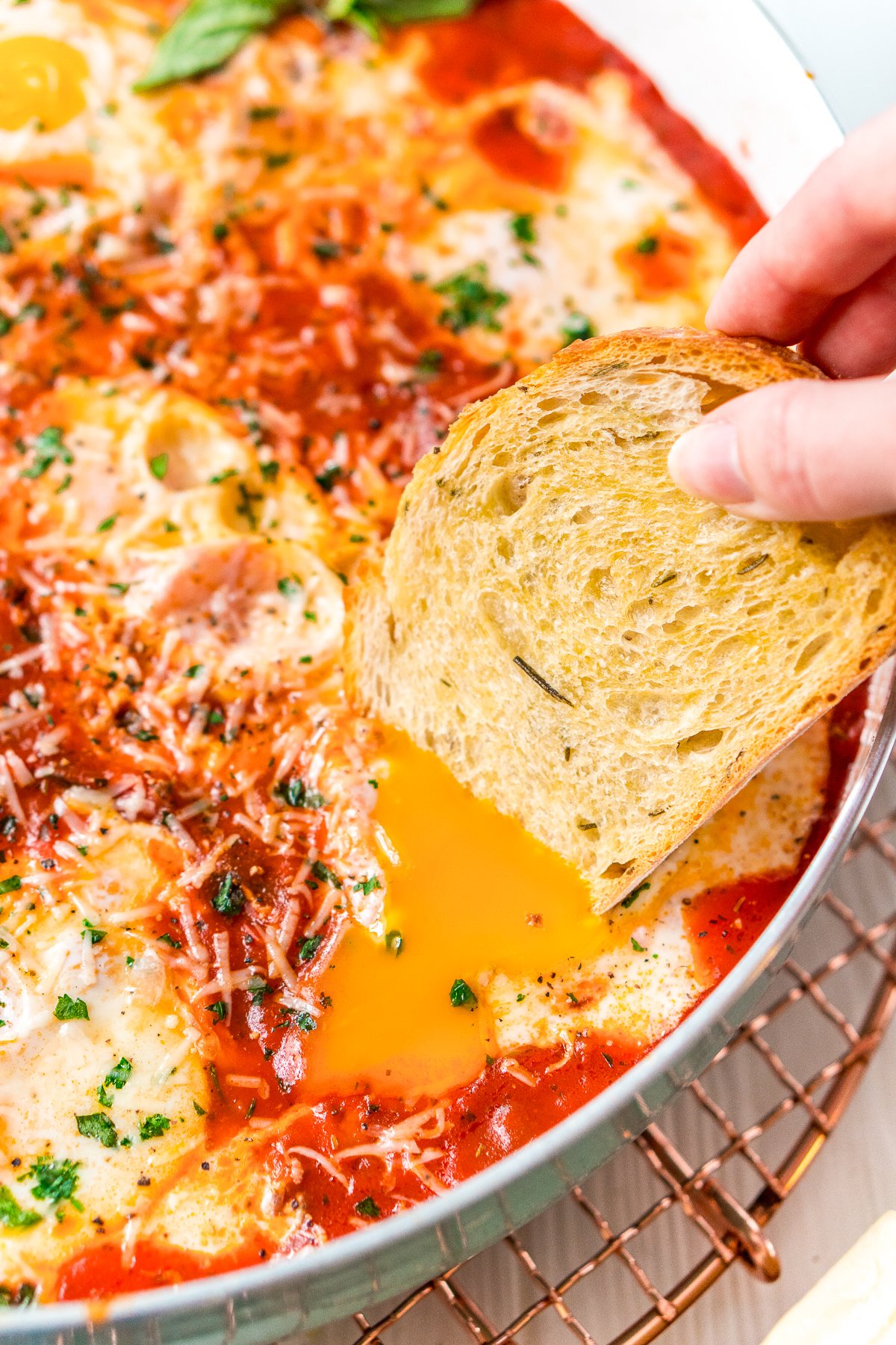 Crusty bread being dipped into a poached egg in a batch of Eggs In Purgatory.