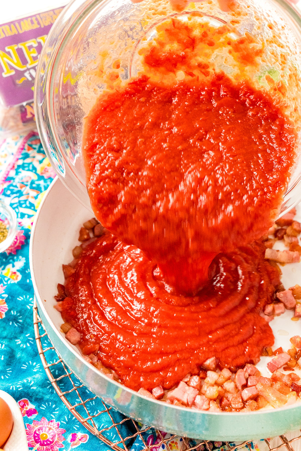 Crushed Tomatoes being added to a skillet with pancetta and garlic.