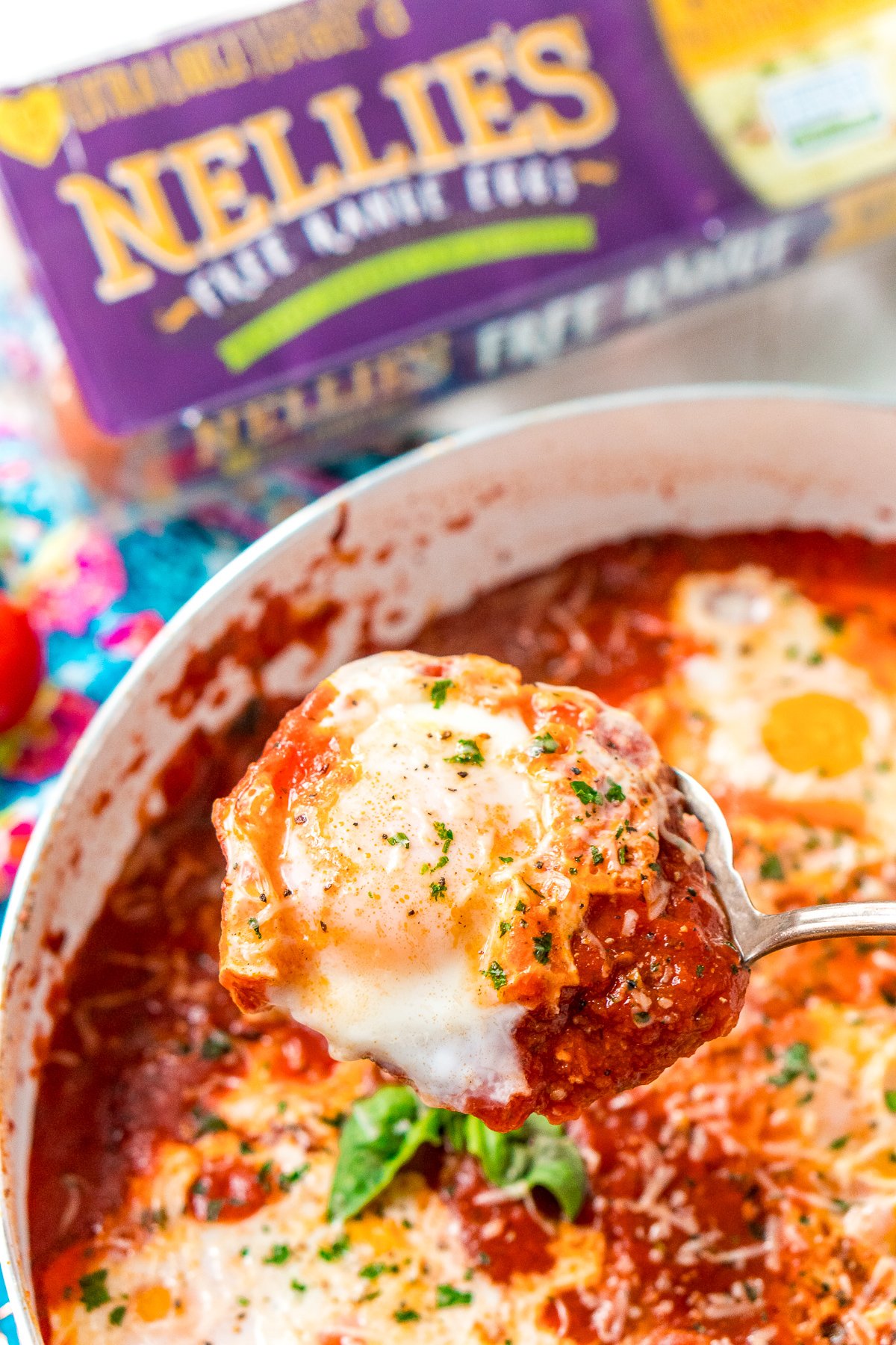 Poached egg being lifted out of Eggs In Purgatory with a serving spoon.