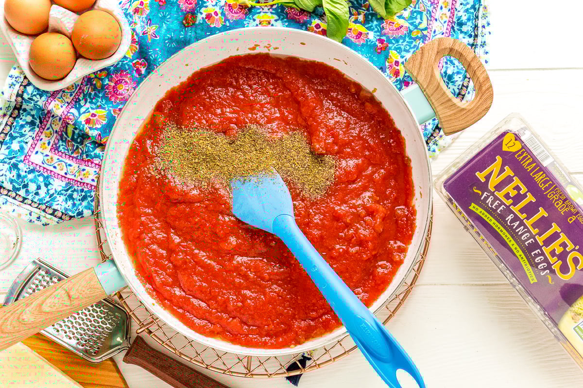 Italian Seasoning being added to a fry pan with tomato sauce.
