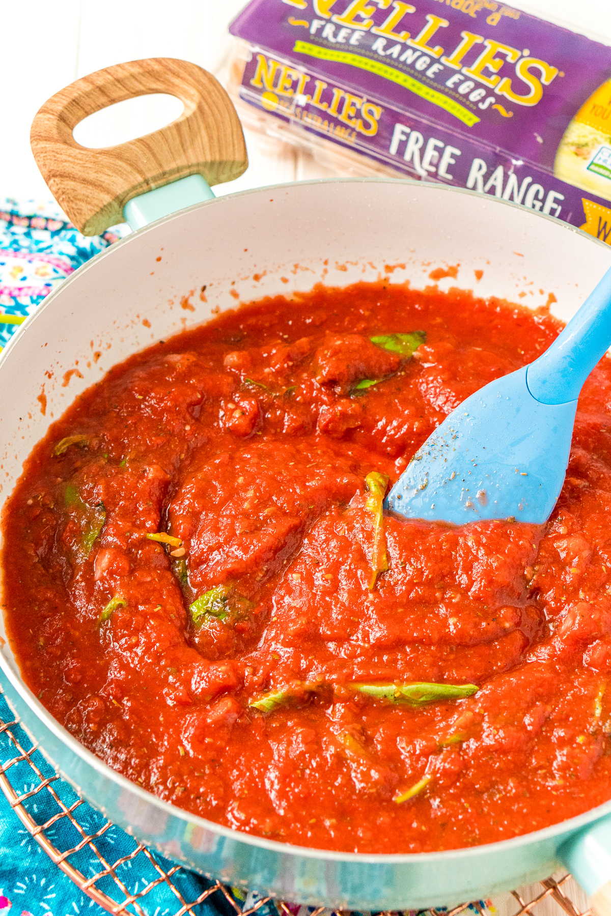 Spinach and basil being stirred into a pan of tomato sauce.