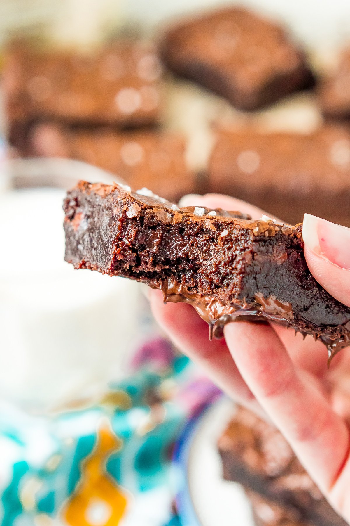 Woman's hand holding a olive oil brownie with a bite taken out of it.