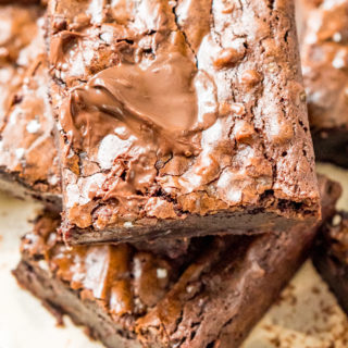 Brownie squares stacked on top of each other on parchment paper.