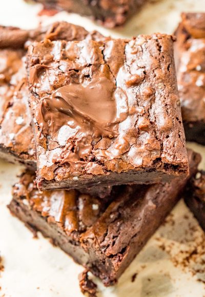 Brownie squares stacked on top of each other on parchment paper.