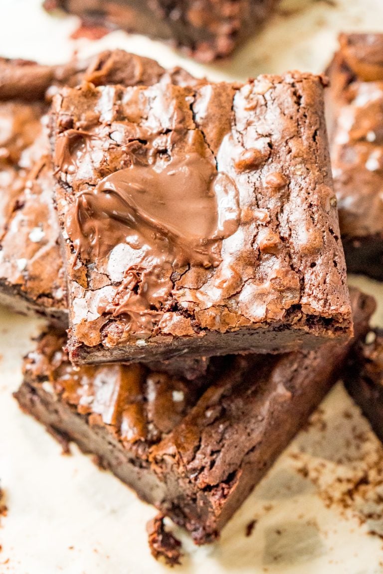 Brownie squares stacked on top of each other on parchment paper.