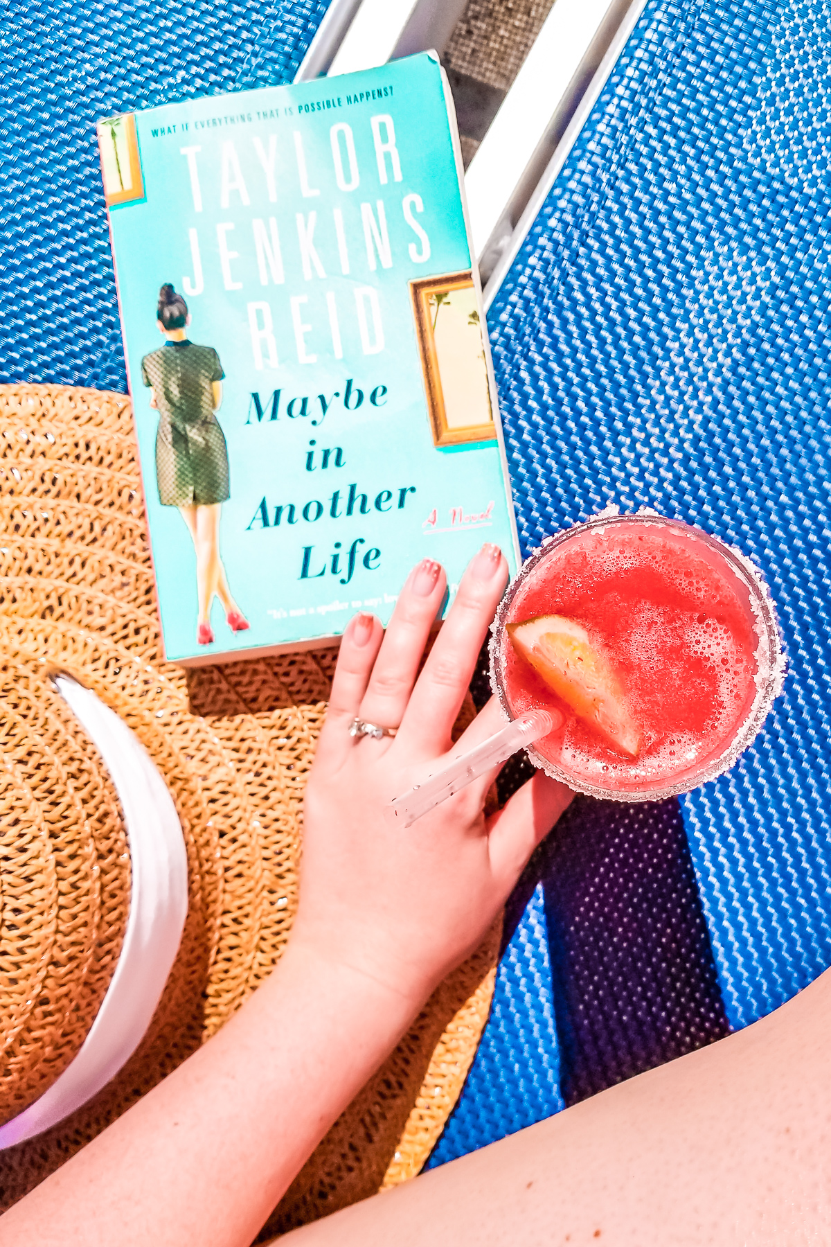 Sunhat, book, and frozen cocktail sitting on a blue lounge chair.