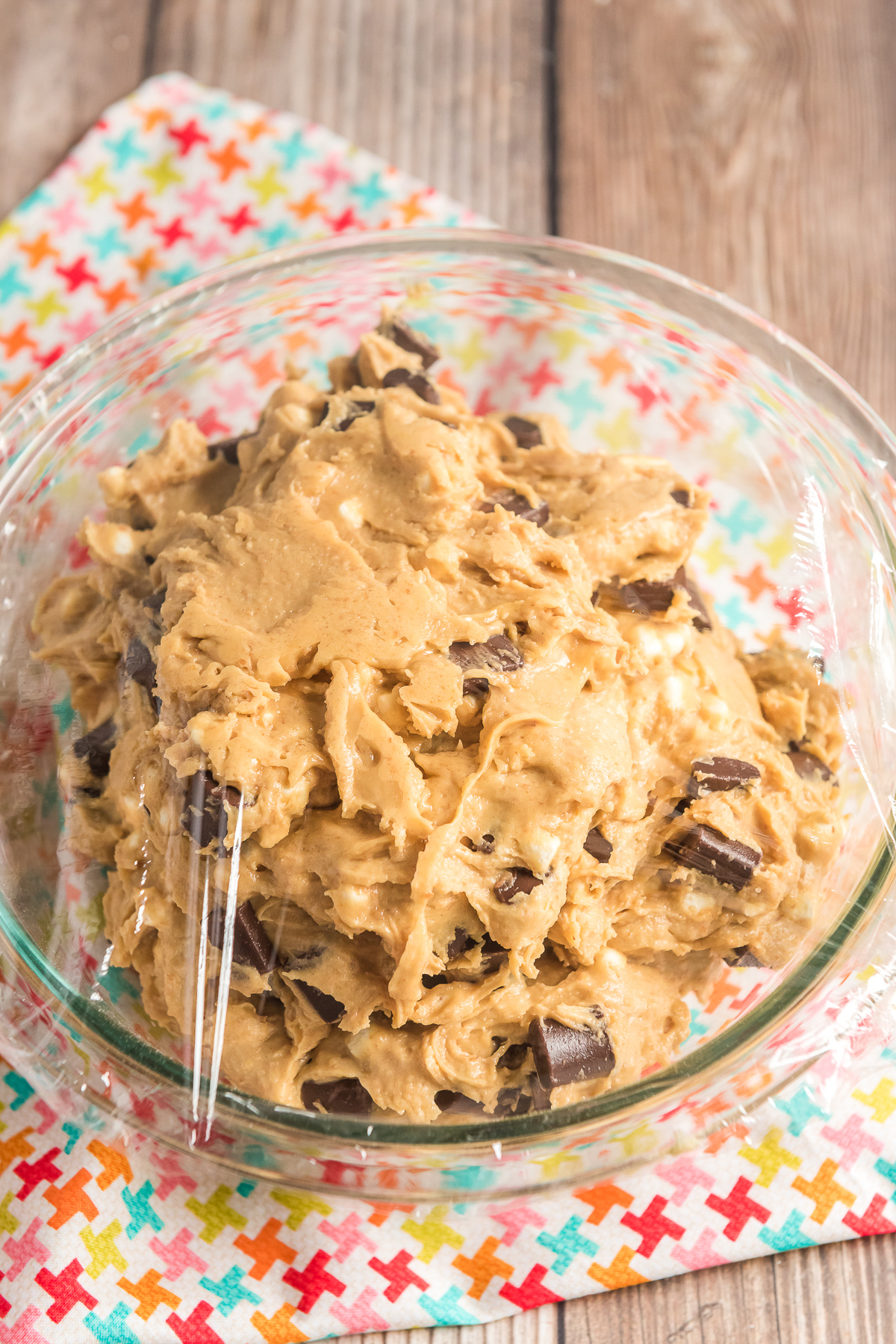 Cookie dough in a glass mixing bowl covered with plastic wrap.