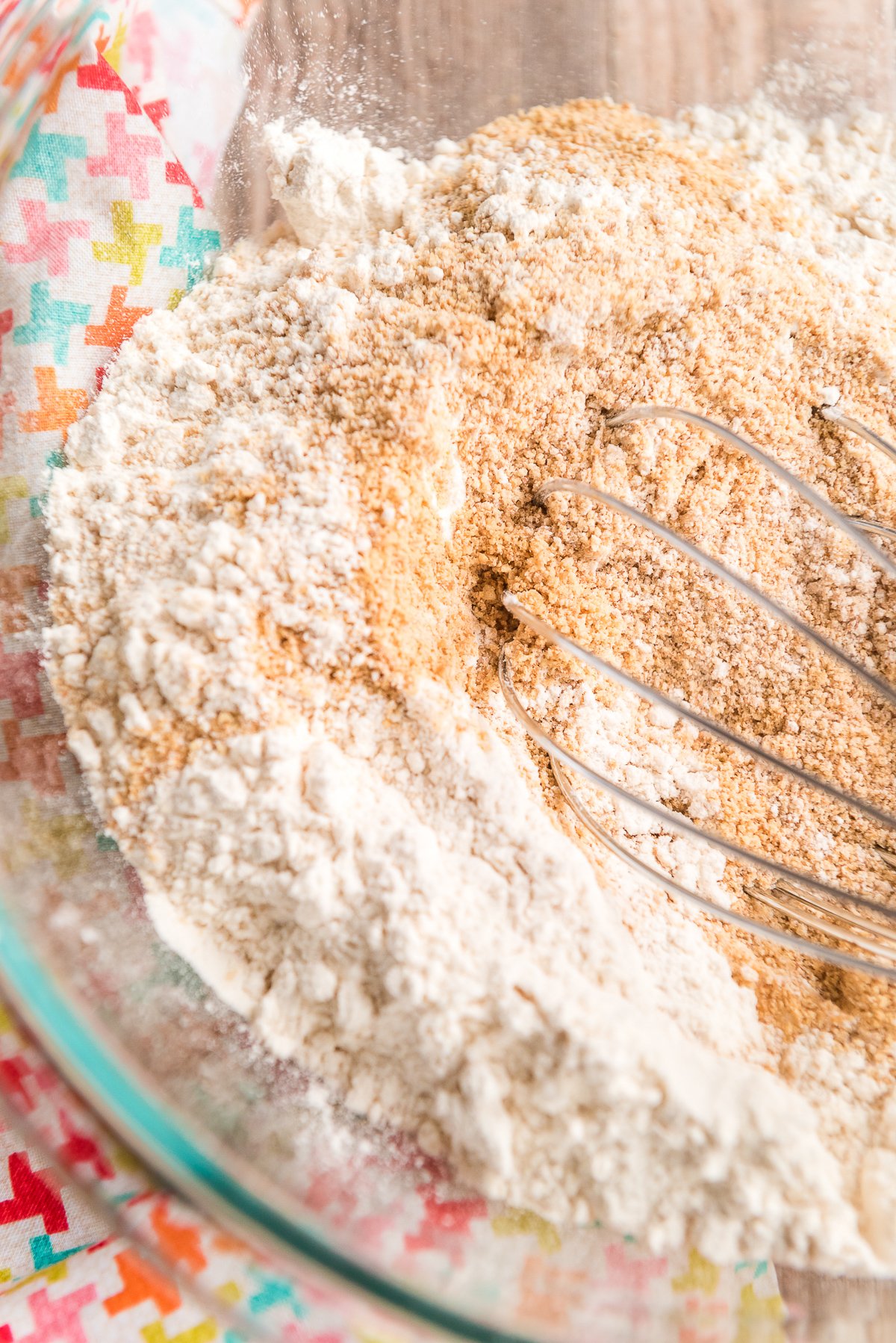 Flour and graham cracker crumbs being whisked together in a glass bowl.