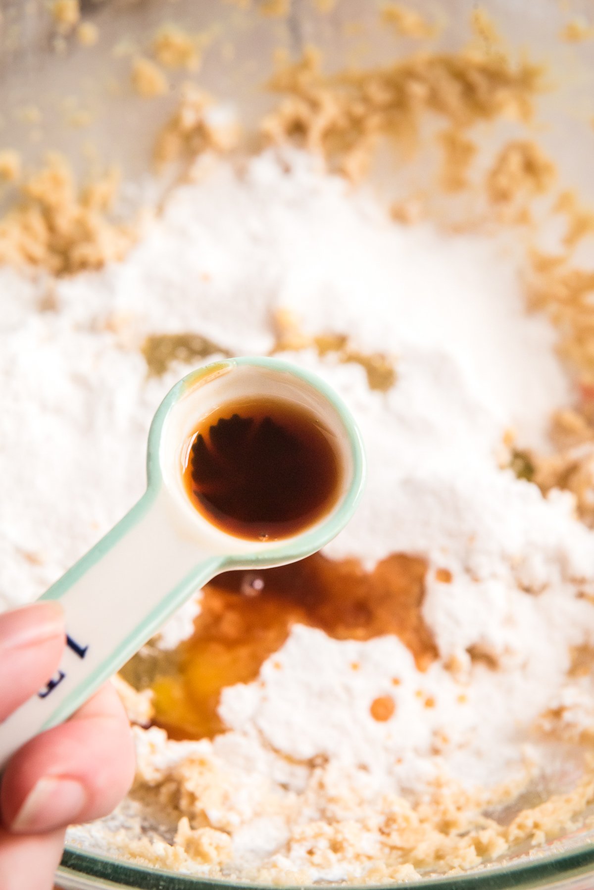 Spoon of vanilla being adding to a mixing bowl.