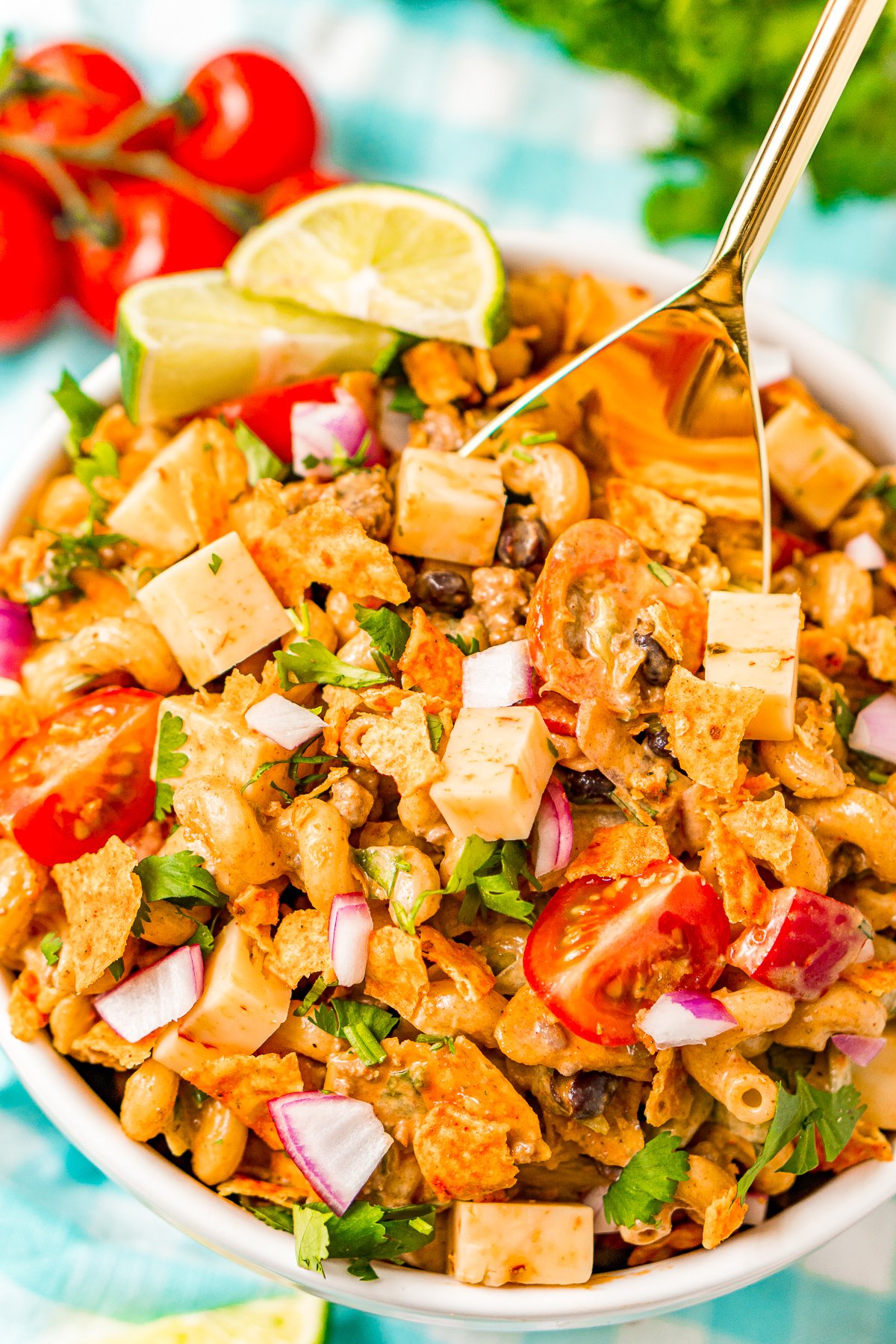 Gold serving spoon scooping up taco pasta salad out of a large white bowl.