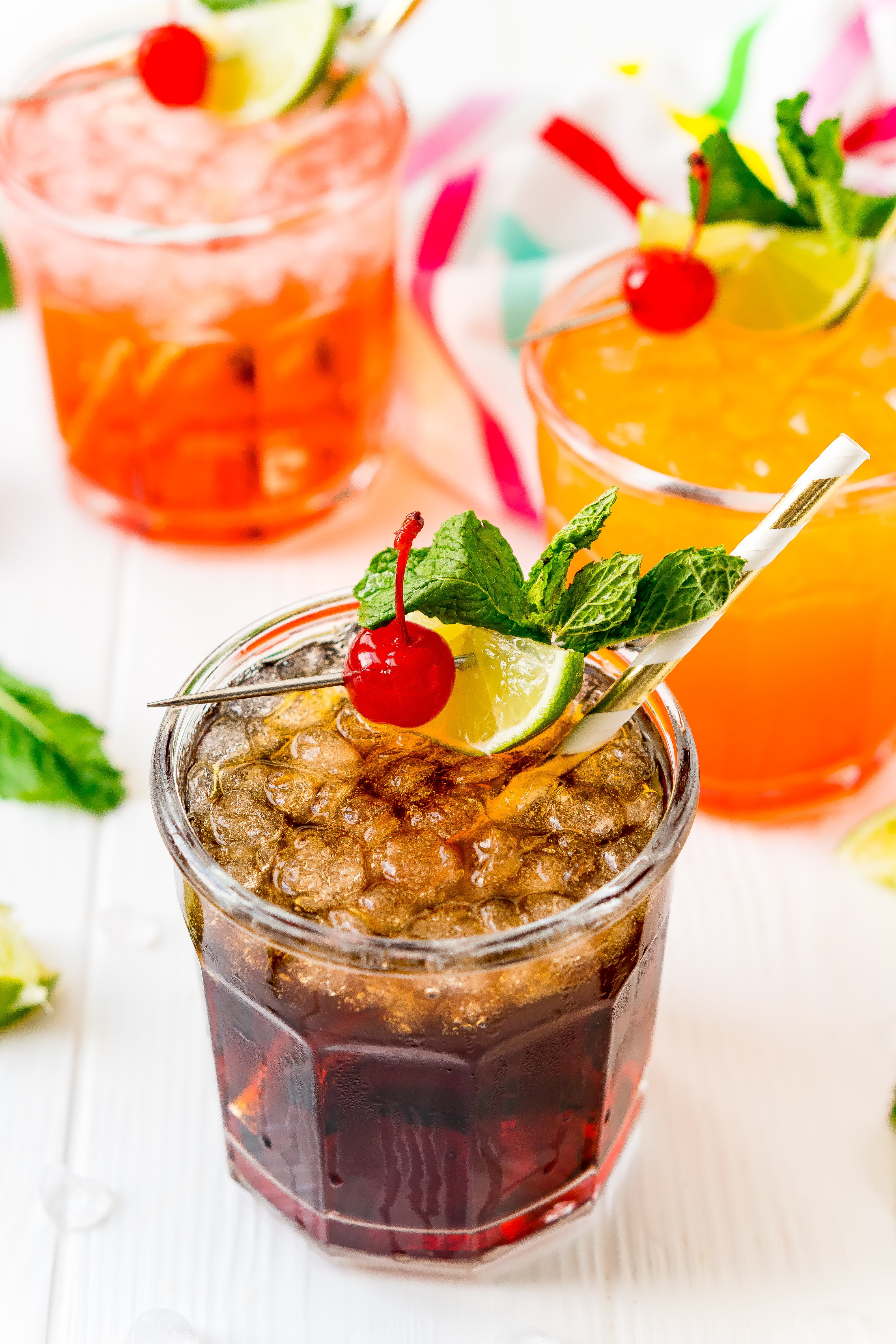 Mocktails in glasses garnished with mint, cherry, and lime.