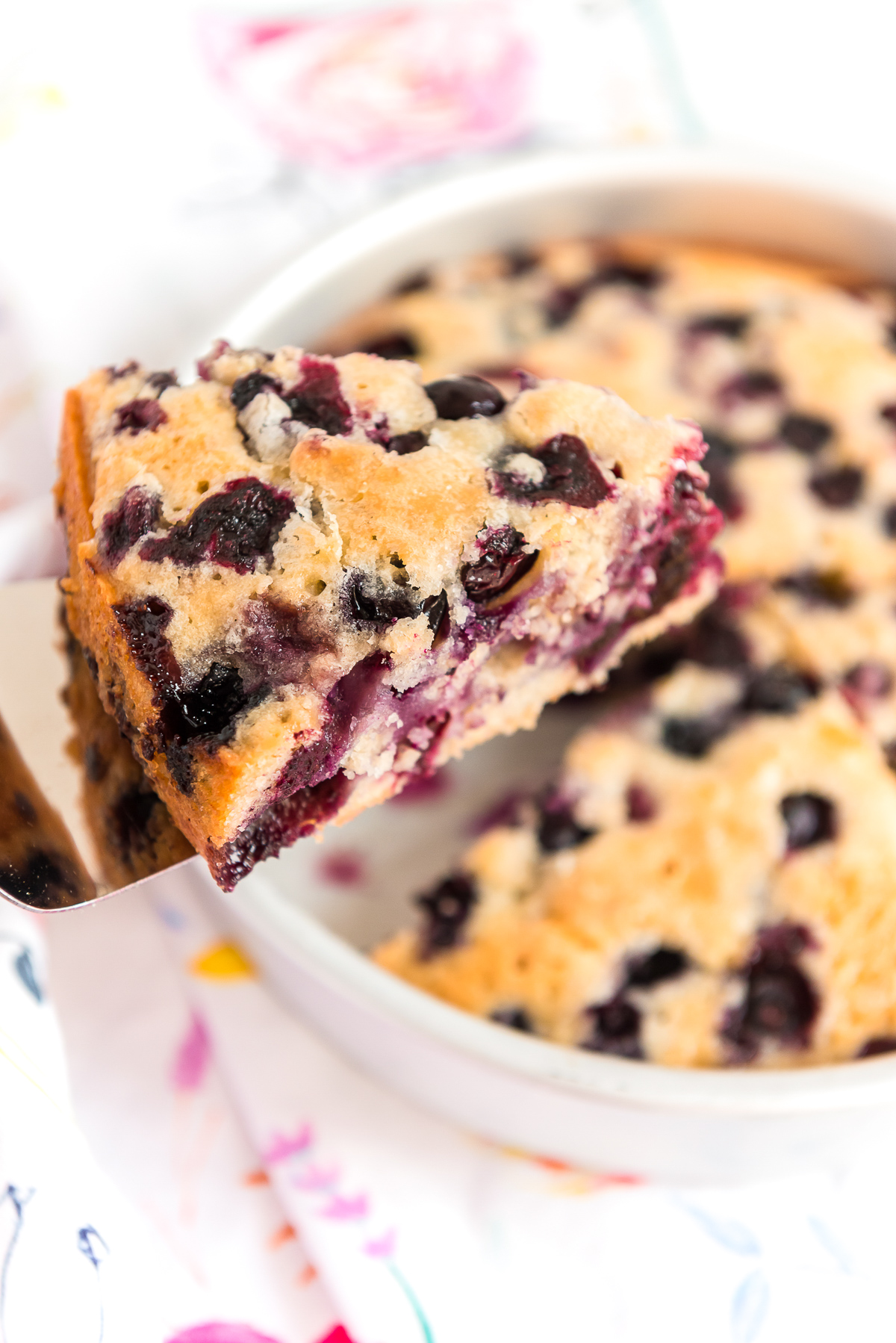 Piece of blueberry cake on a server being lifted out of the cake pan.