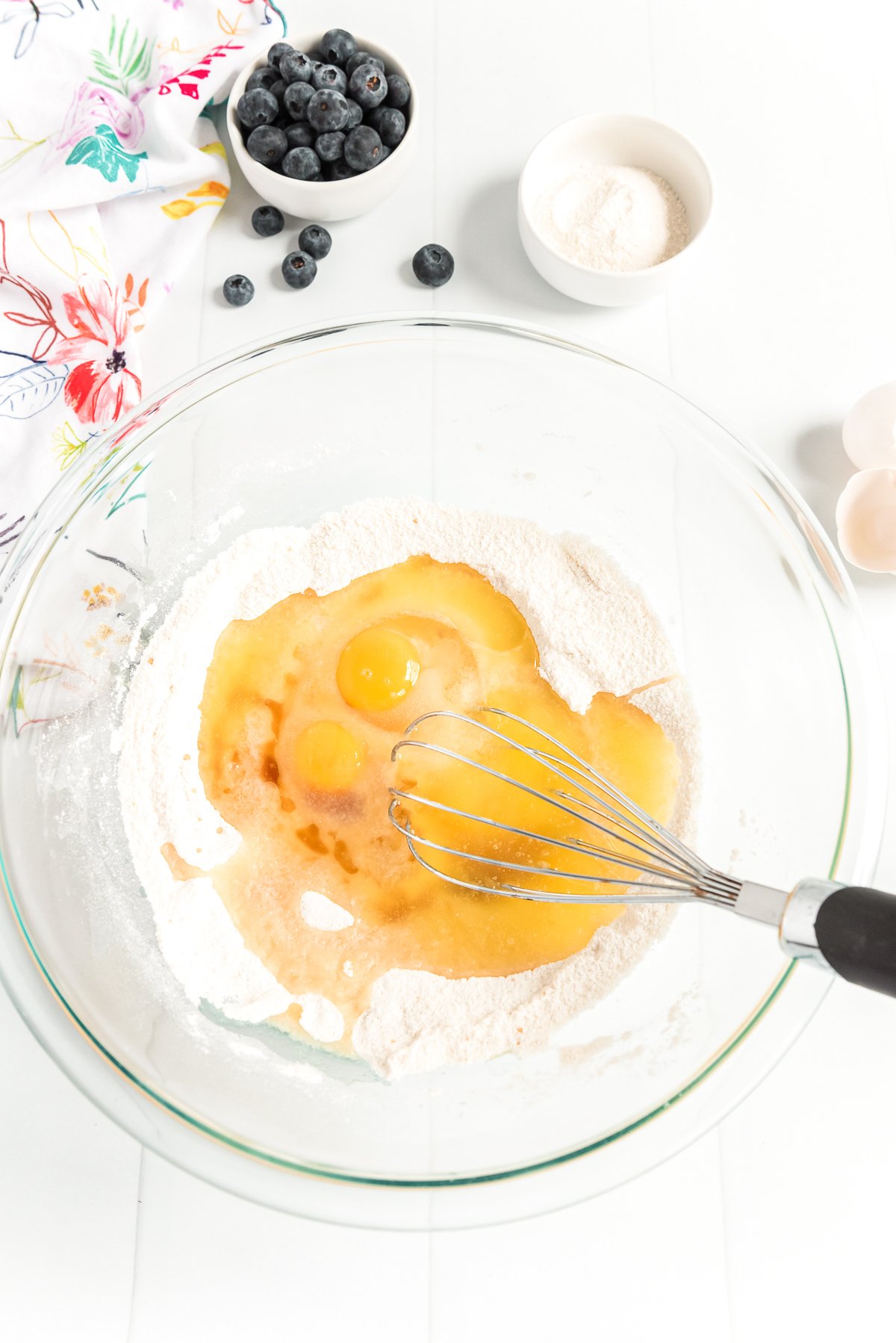 Eggs being mixed into flour and sugar in a large glass bowl.