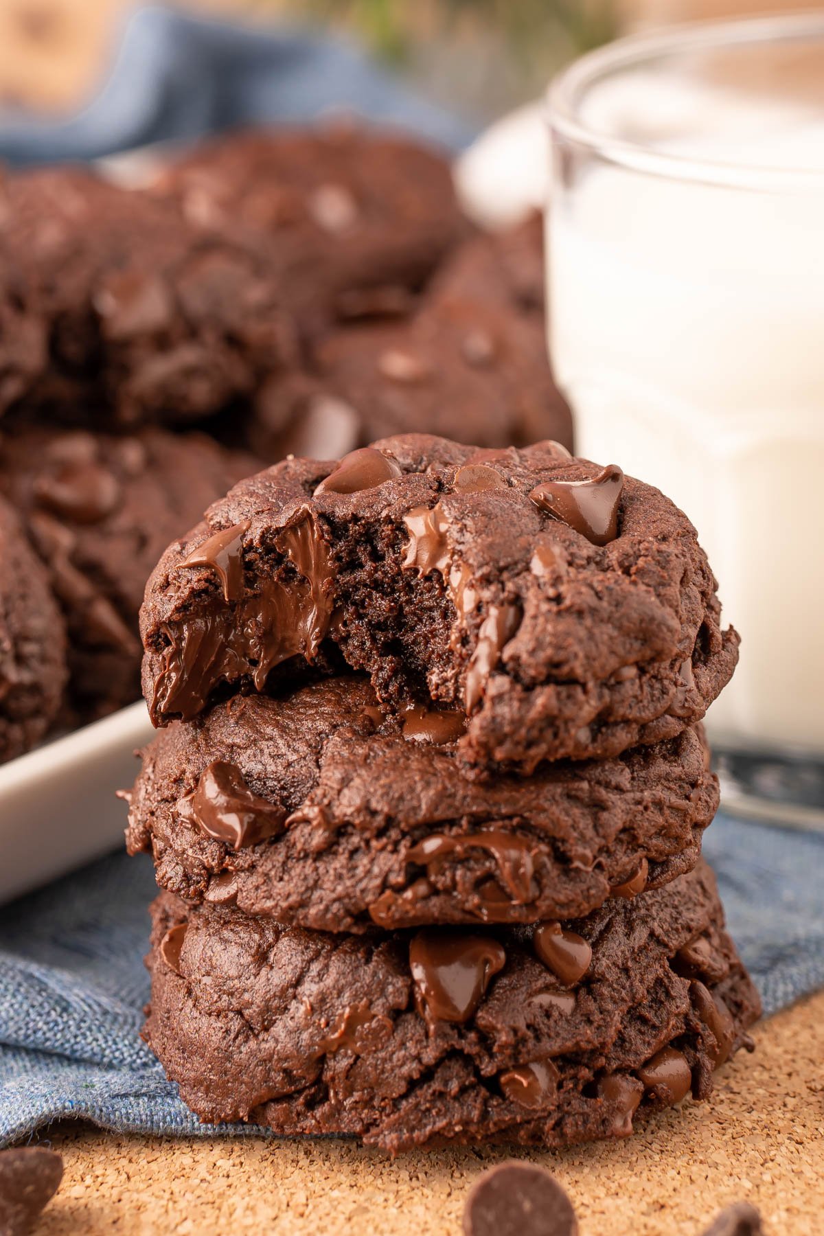 A stack of three double chocolate chip cookies on a blue napkin with the top one missing a bite.