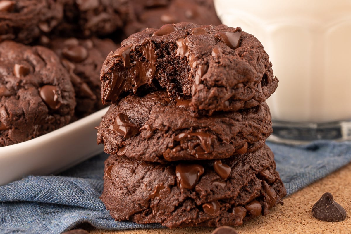 A stack of three double chocolate chip cookies on a blue napkin with the top one missing a bite.