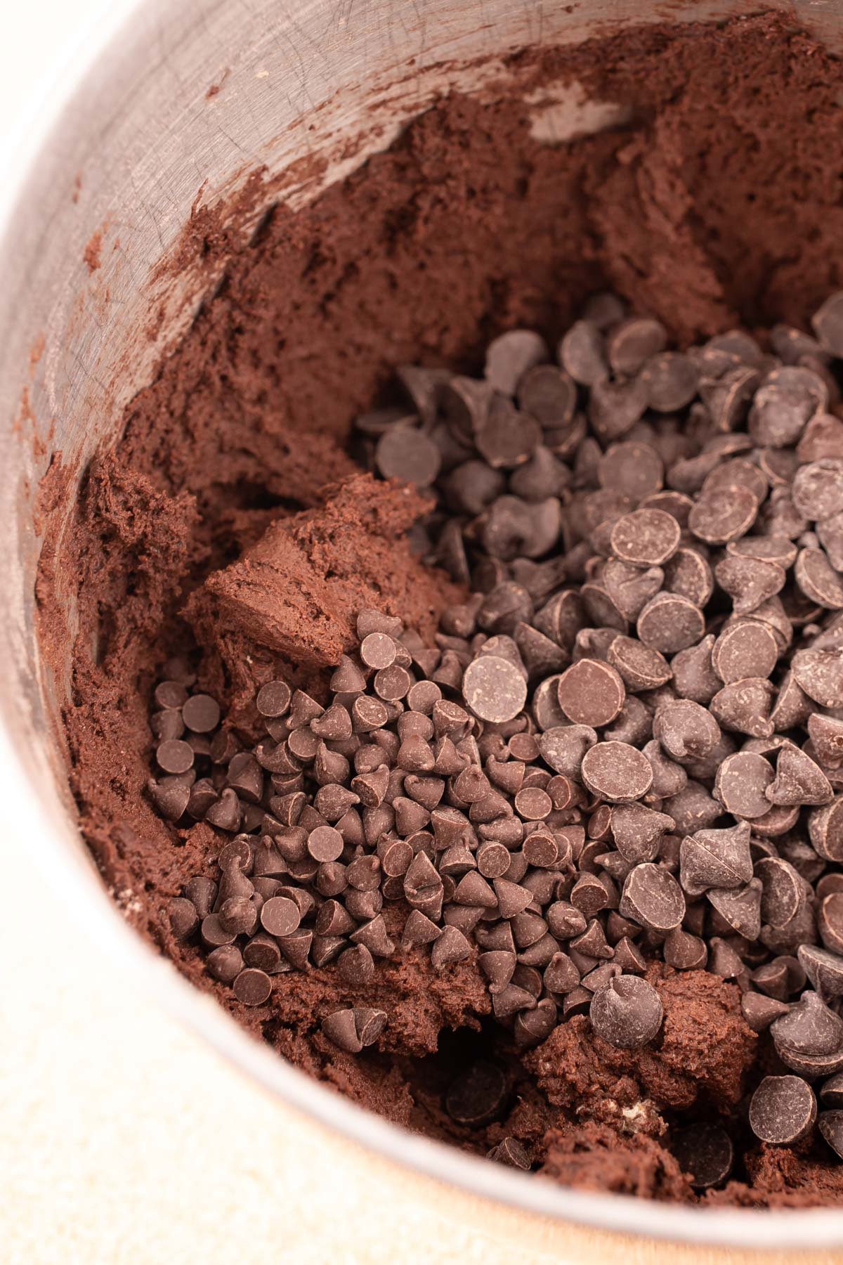 Chocolate chips being added to a stand mixer bowl with chocolate cookie dough.