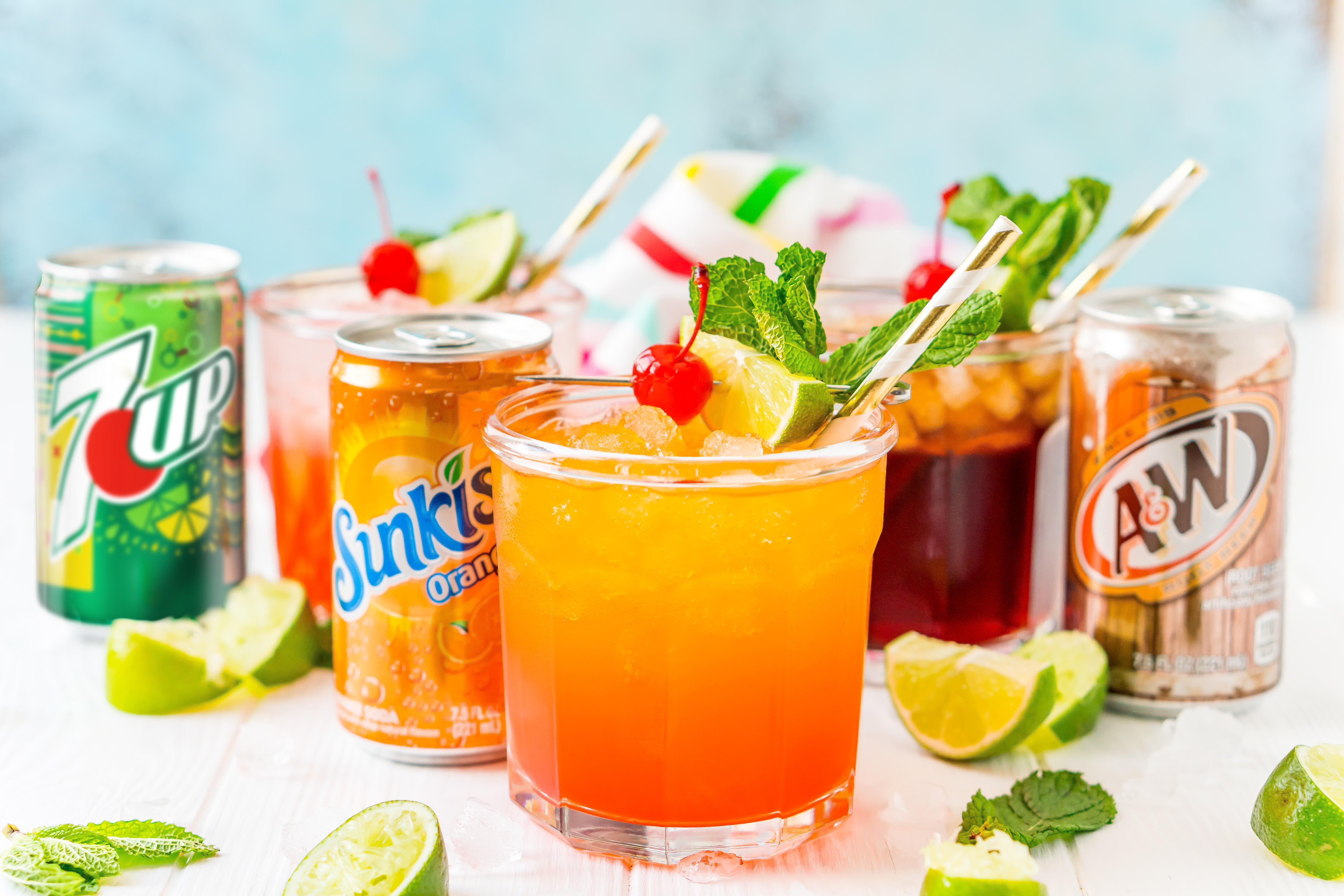 Drinks lined up with garnishes and soda cans next to them.