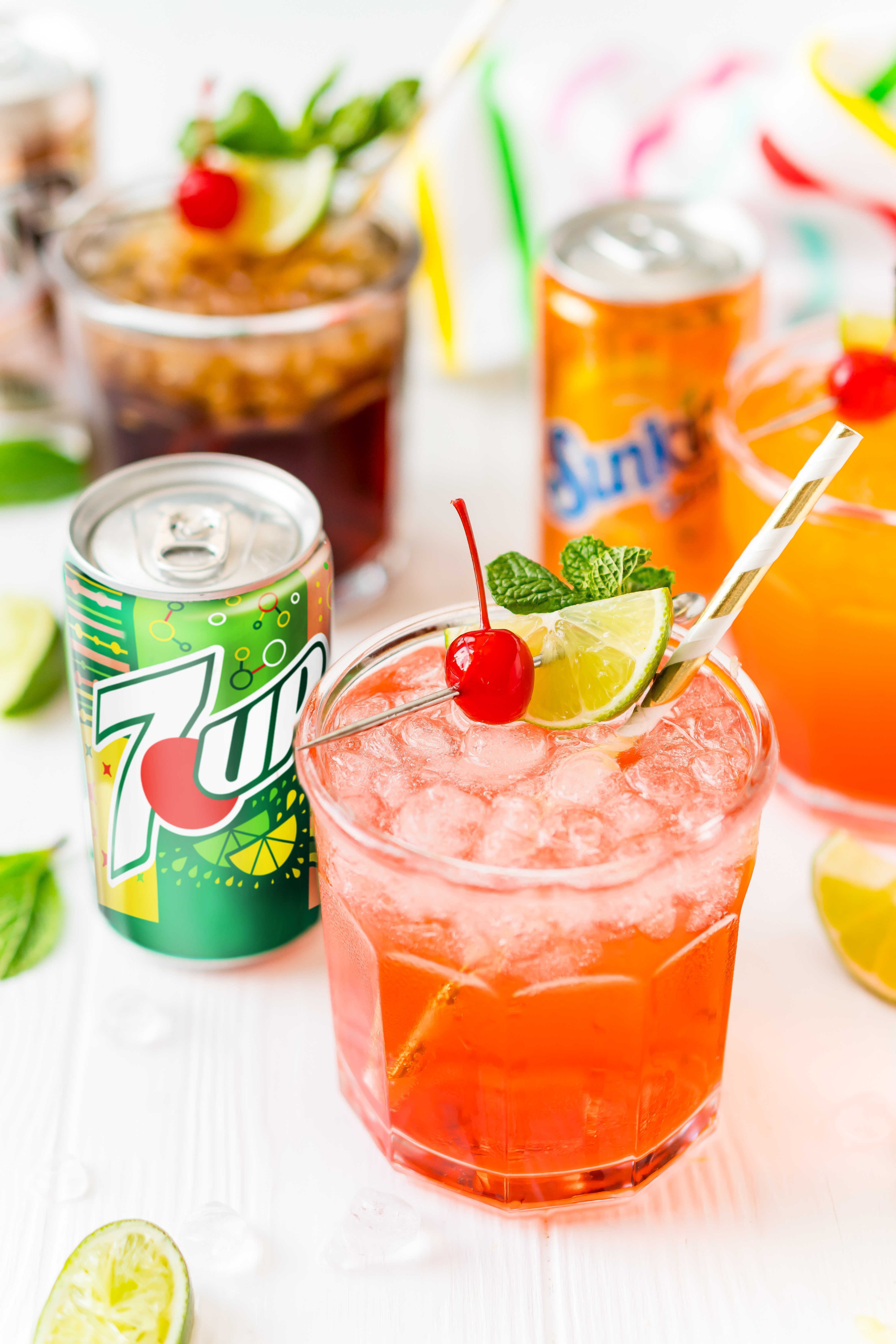 Mocktail in a glass with a can of 7UP next to it and more drinks in the background.