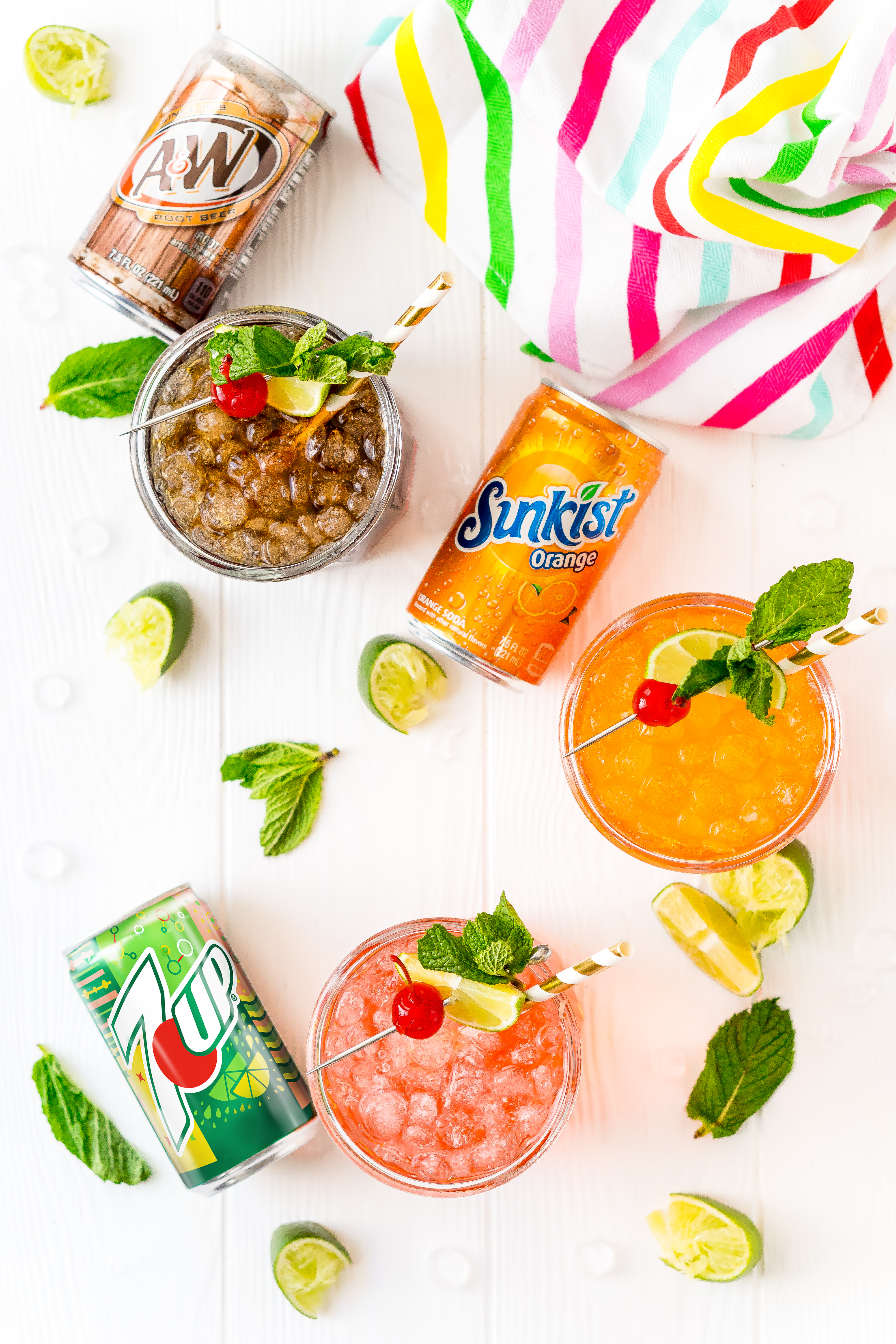 Overhead shot of drinks with cans of soda next to them with lime wedges.