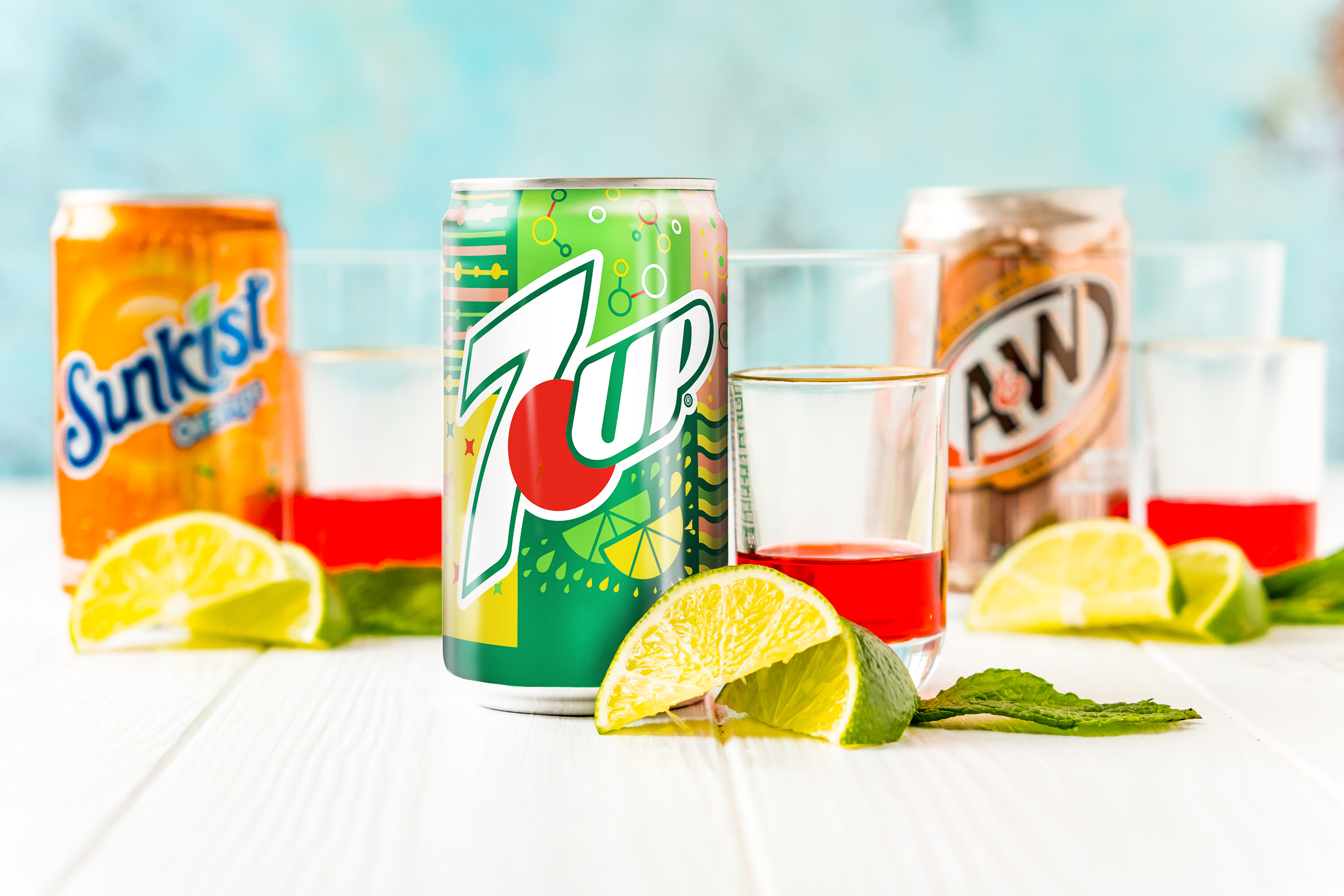 Cans of soda with other drink ingredients next to them on a white counter.