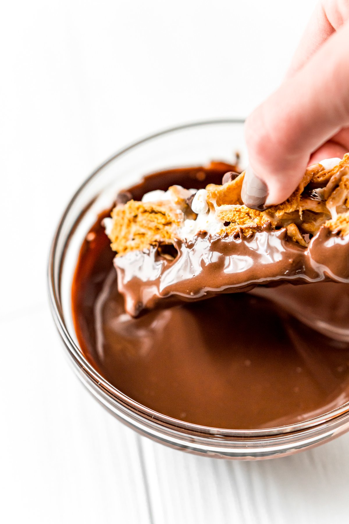 Woman's hand dipping a golden grahams bar in melted chocolate.