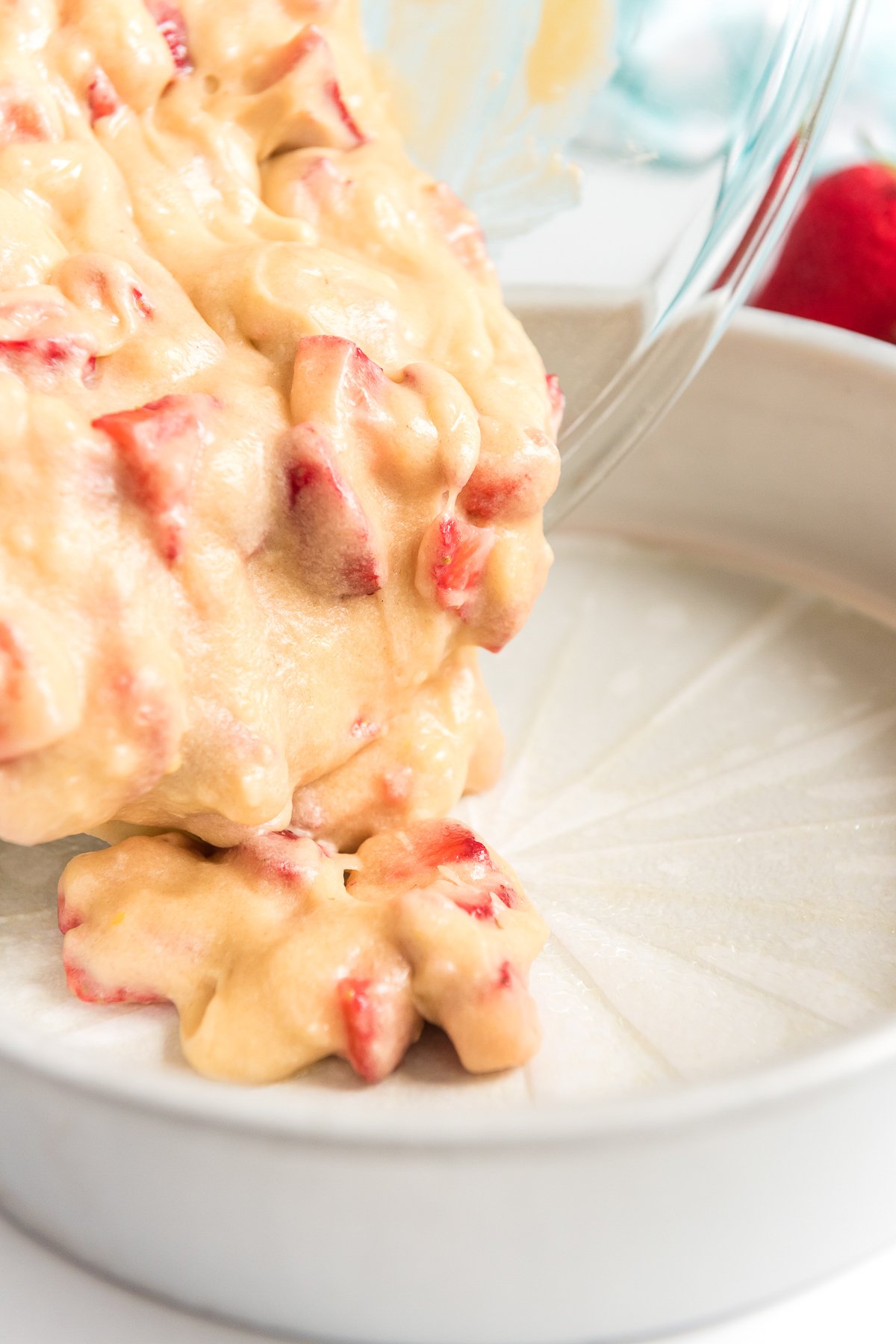 Strawberry cake batter being poured into a prepared cake pan.