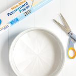 Parchment paper lined cake pan with a roll of parchment paper and pair of scissors next to it.