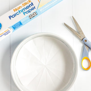 Parchment paper lined cake pan with a roll of parchment paper and pair of scissors next to it.