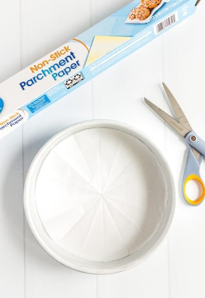 Parchment paper lined cake pan with a roll of parchment paper and pair of scissors next to it.
