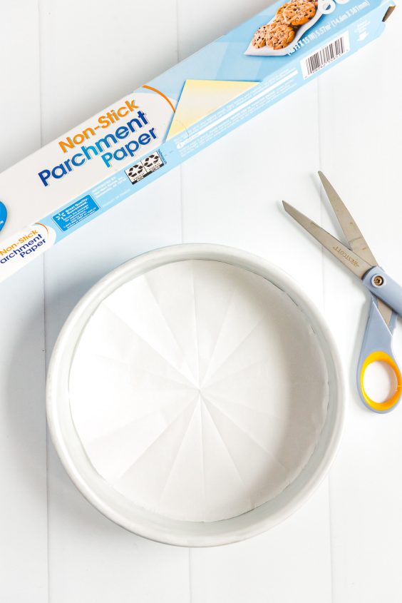 Parchment paper lined cake pan with a roll of parchment paper and pair of scissors next to it.