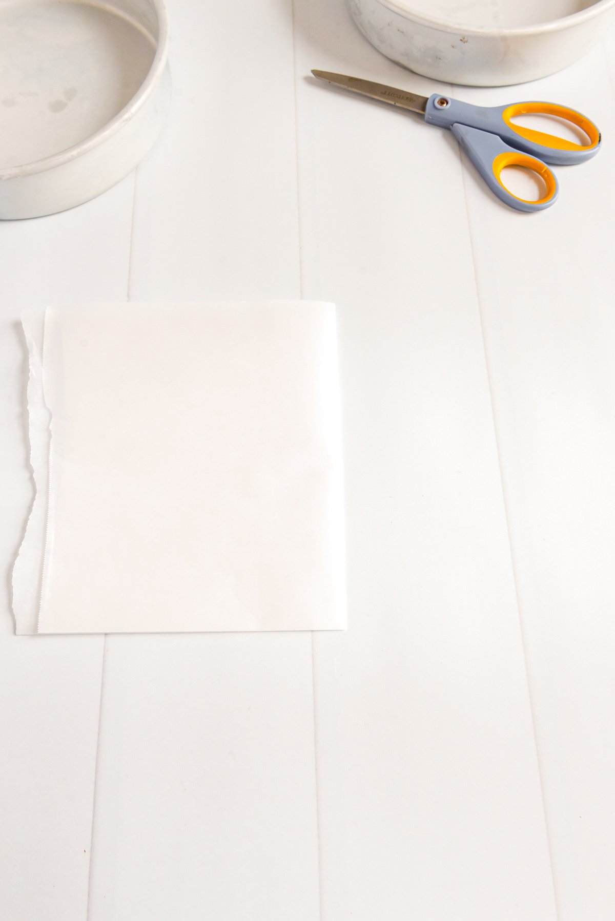 Piece of parchment paper folding in half with cake pans and scissors on the table.