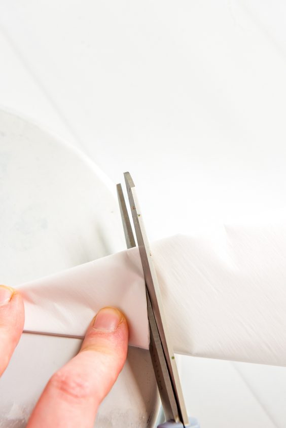 Folded parchment paper being cut to line a cake pan.