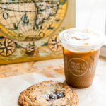 Chocolate chip cookies and a to-go iced coffee sitting on a wooden counter.