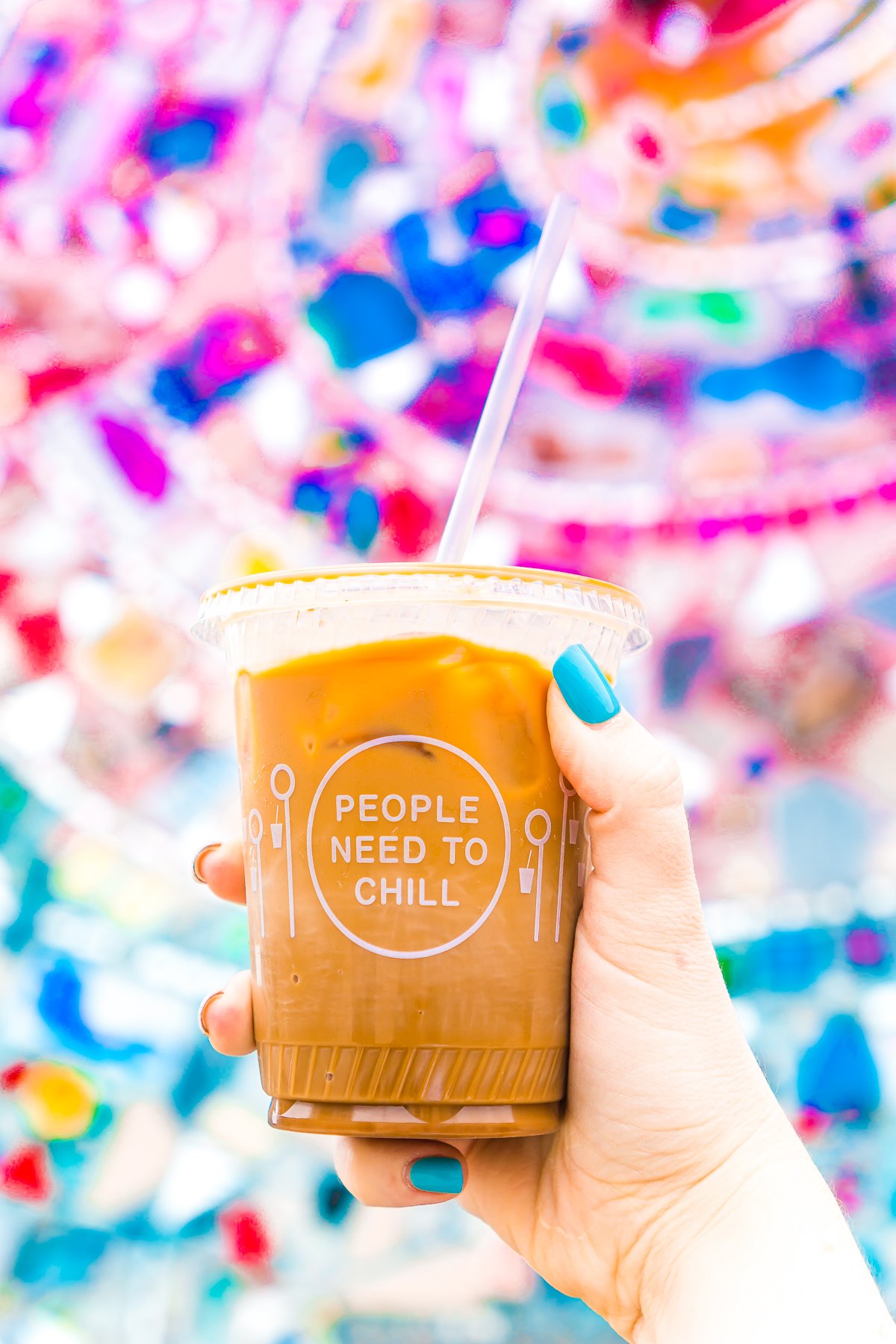 Woman's hand holding up a cup of iced coffee in front of a colorful mural in Portland, ME.