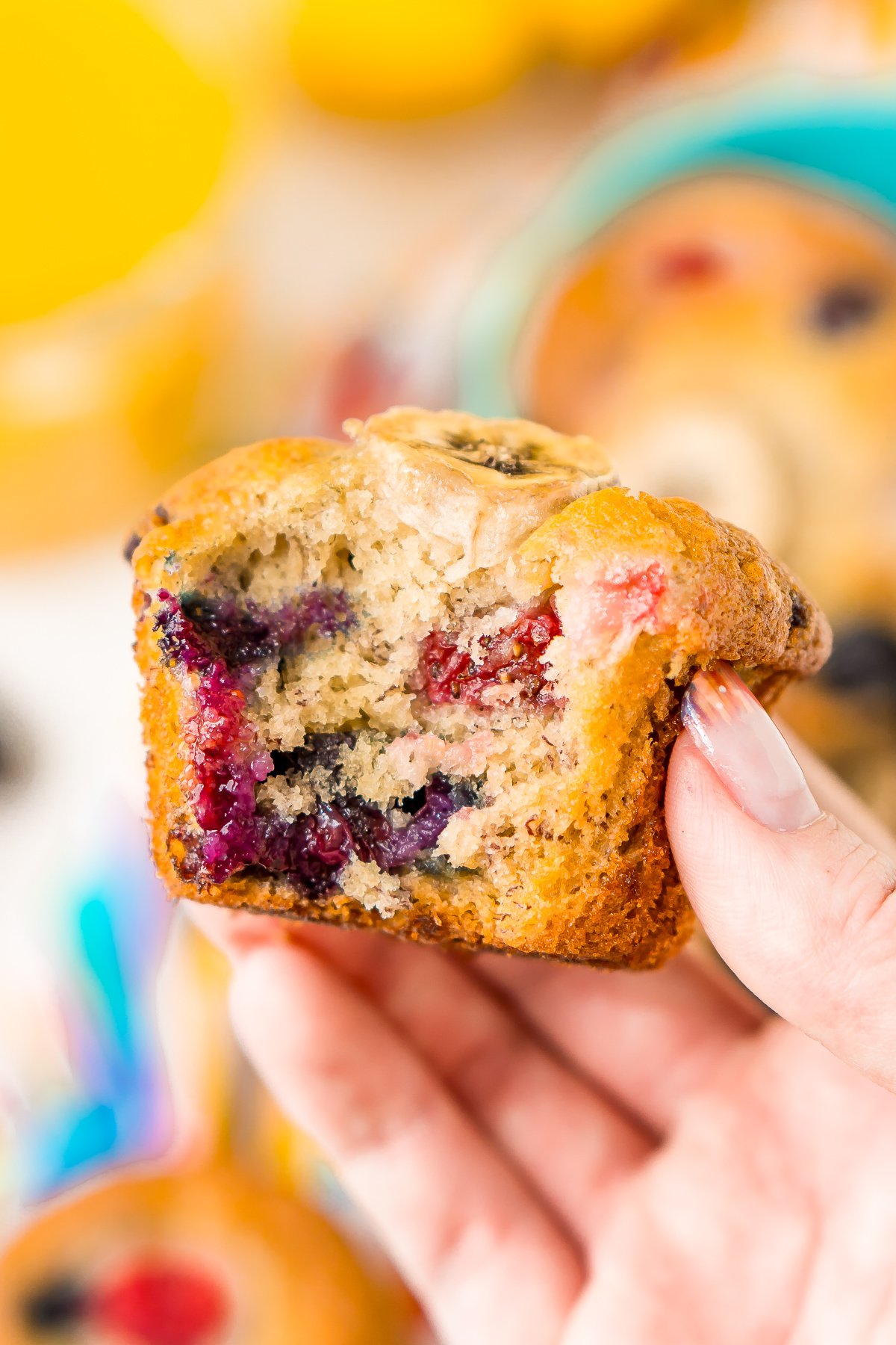Close up photo of a woman's hand holding a banana berry muffins with a bite taken out of it.