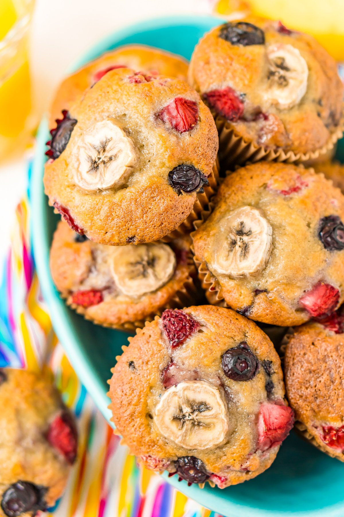 Muffins with banana and berries piled in a teal bowl.