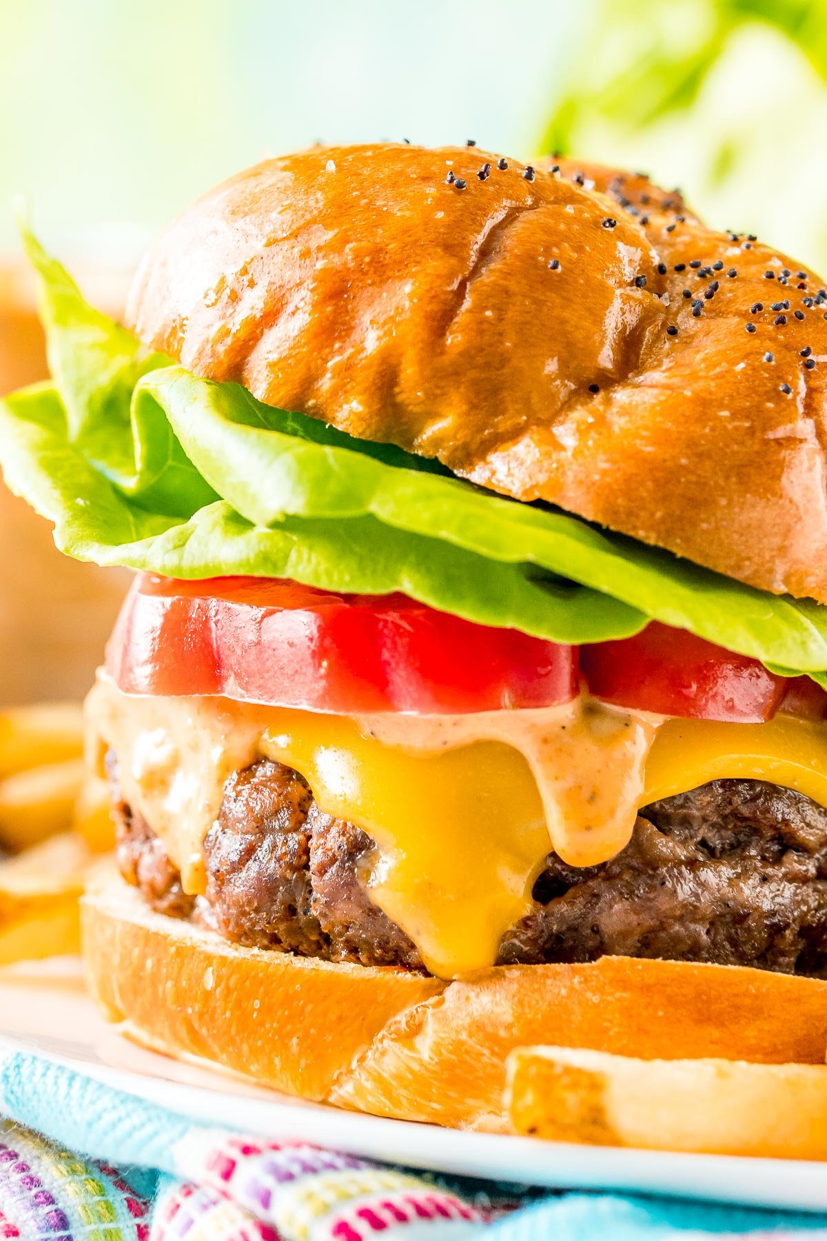 Close up photo of a juice burger topped with cheese, sauce, tomato, and lettuce.