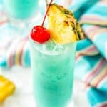 Angled close up photo of a blue hawaiian cocktail garnished with a pineapple edge and cherry.