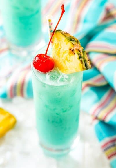 Angled close up photo of a blue hawaiian cocktail garnished with a pineapple edge and cherry.