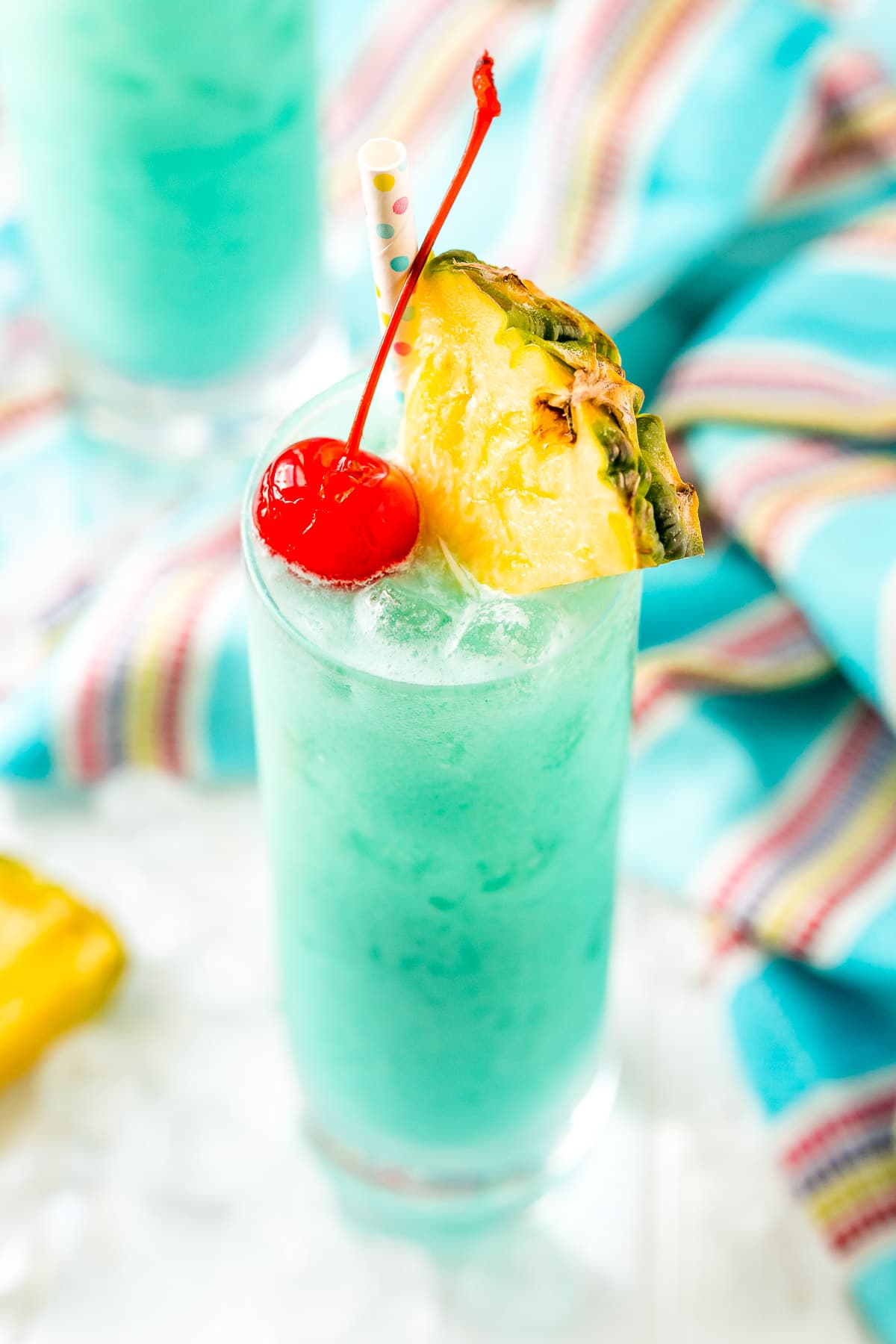 Angled close up photo of a blue hawaiian cocktail garnished with a pineapple edge and cherry.