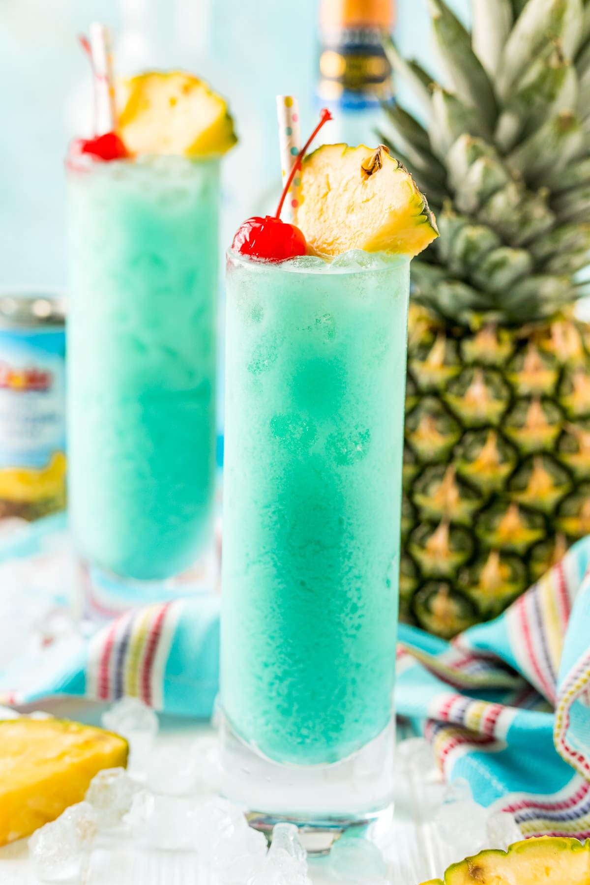 Close up photos of two classes filled with a blue cocktail with a pineapple in the background.
